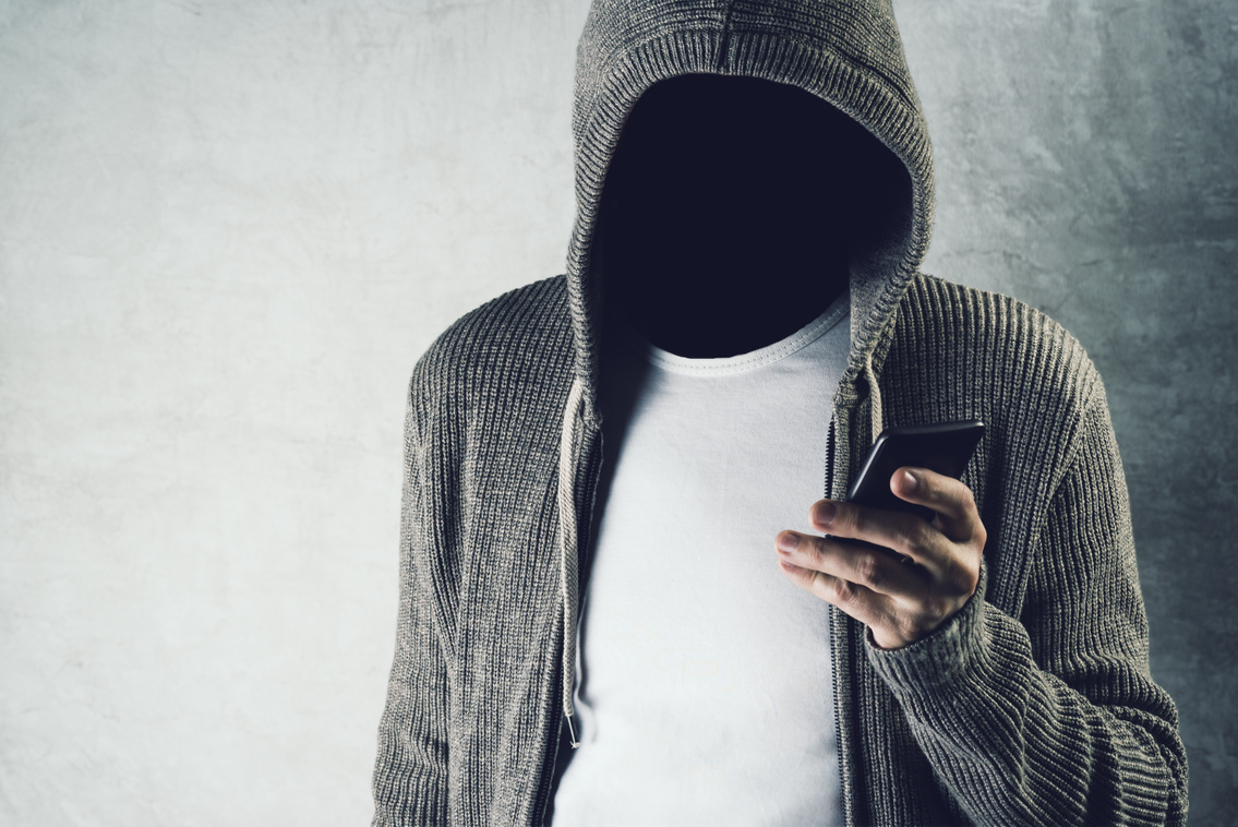 Faceless hooded person using mobile phone, identity theft concept